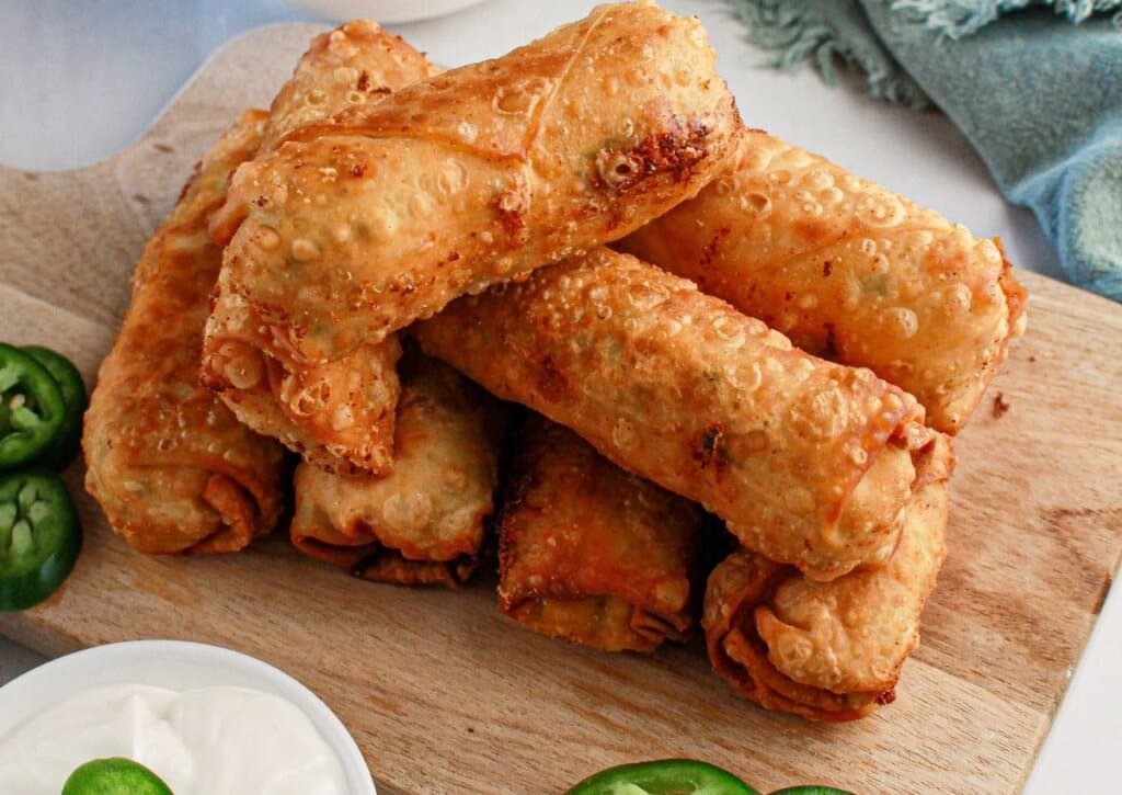 Egg rolls stacked on wooden cutting board.