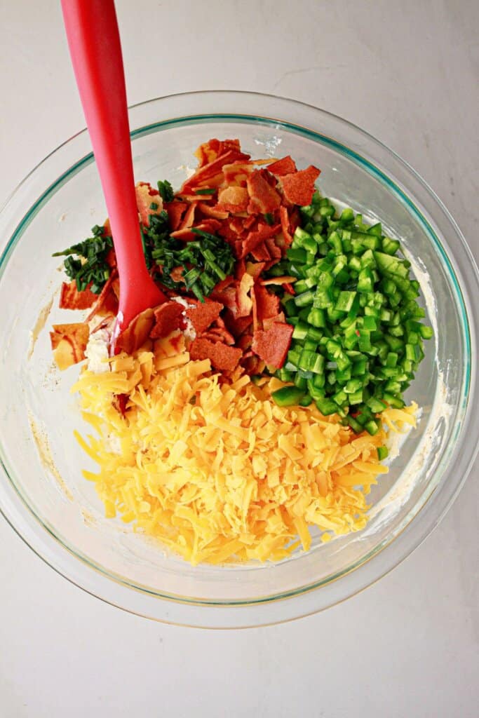 Cheese, bacon, peppers, chives, and cream cheese in a glass bowl.