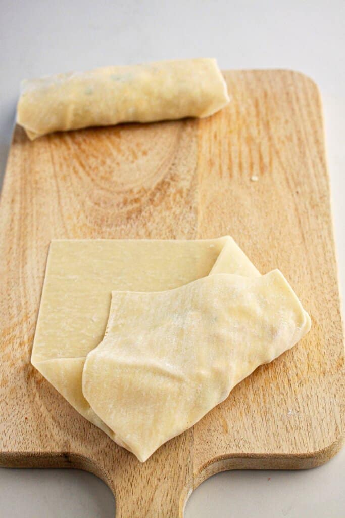 Egg roll being wrapped on a cutting board.