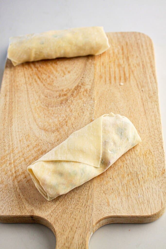 Sealed egg roll on a wooden cutting board.