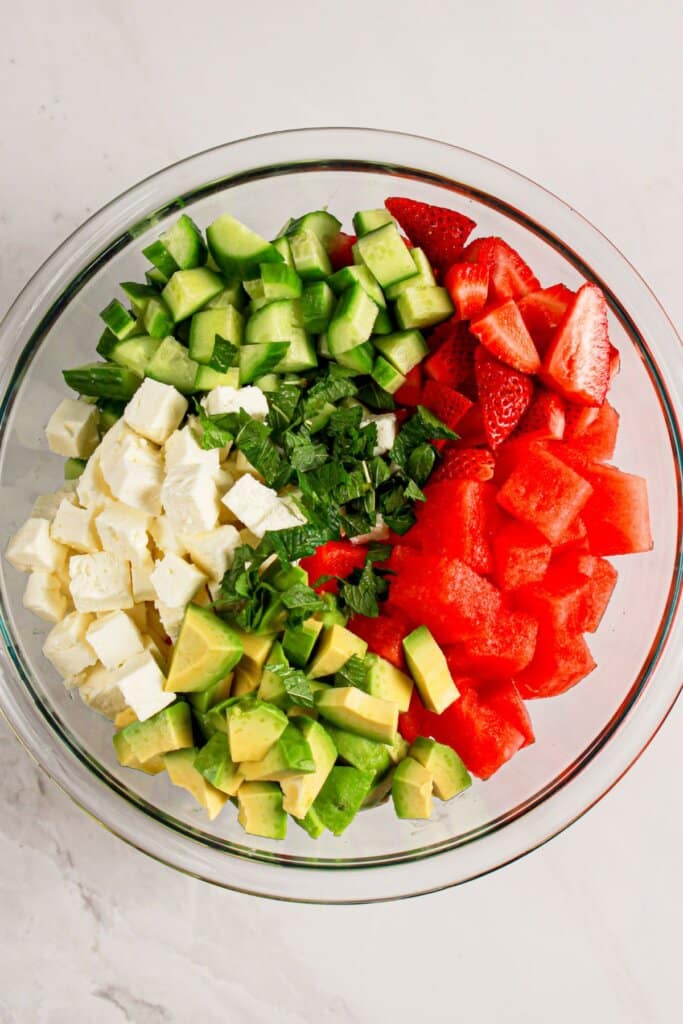 Glass bowl full of fruit, cheese, and mint.