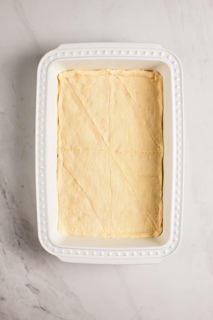 Crescent rolls being pressed into a baking dish.