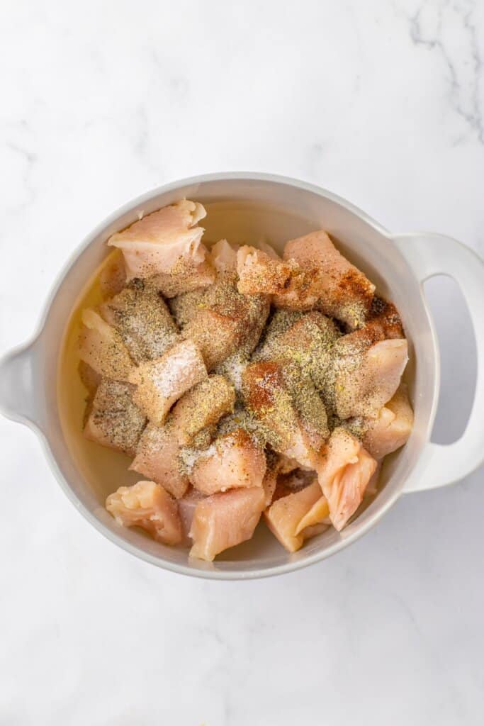 Meat being seasoned in a large bowl.