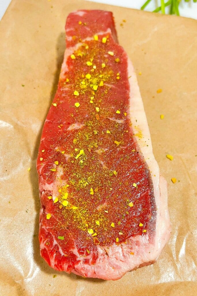 Meat being seasoned on parchment paper.
