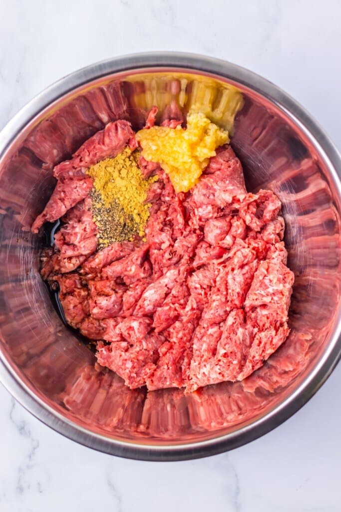 Ground beef, garlic and seasonings being mixed in a bowl.