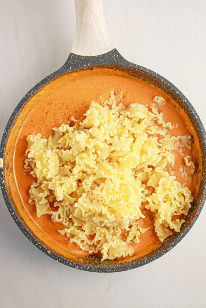 Cooked noodles being added to sauce in a pan.
