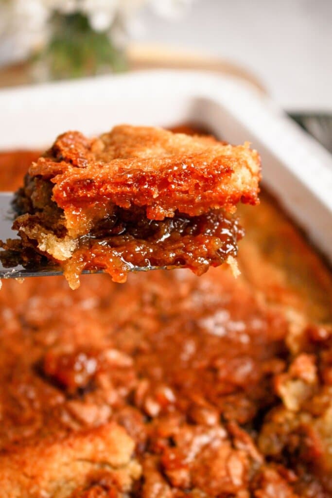 Scoop of pecan pie cobbler above a baking dish.