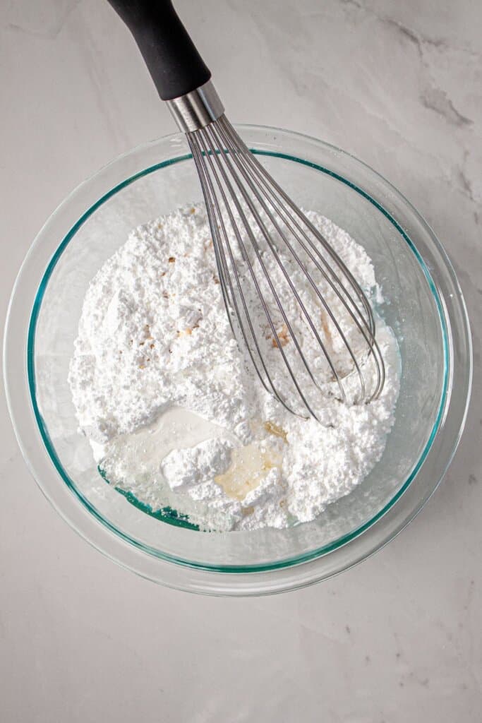 Powdered sugar and wet ingredients being mixed in a glass bowl.