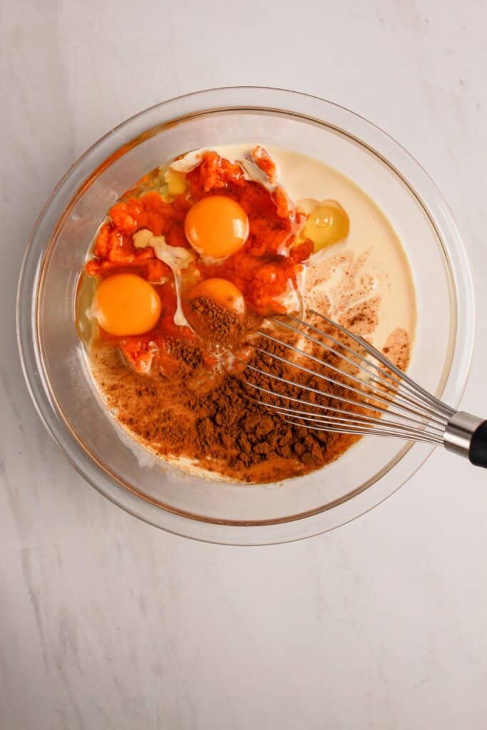Eggs and pumpkin being mixed in a glass mixing bowl.