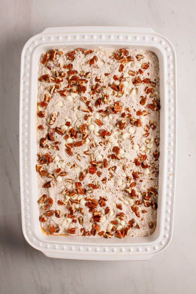 Pecans and white chocolates being sprinkled on top of a dessert.