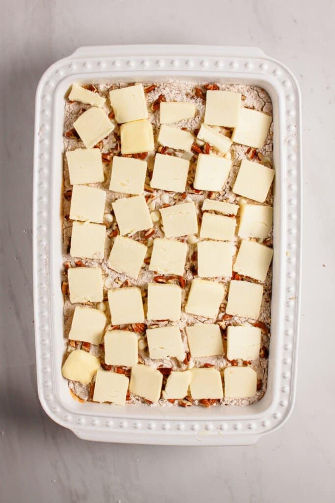 Butter slices being placed on top of a baking dish.