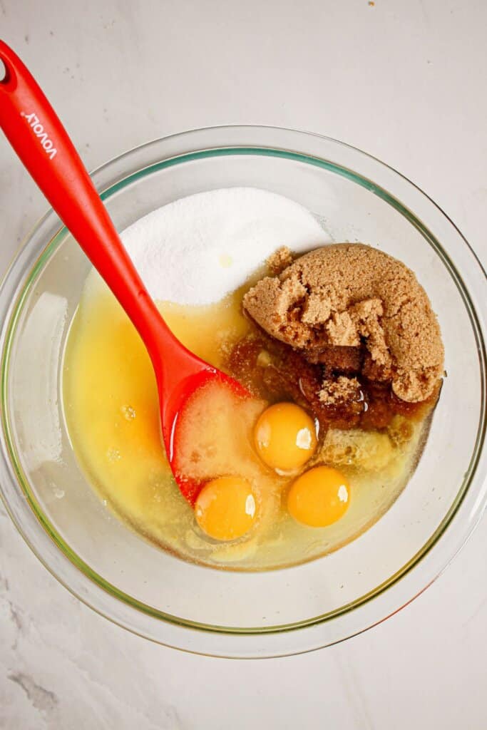 Eggs, brown sugar, and sugar being mixed in a glass bowl.