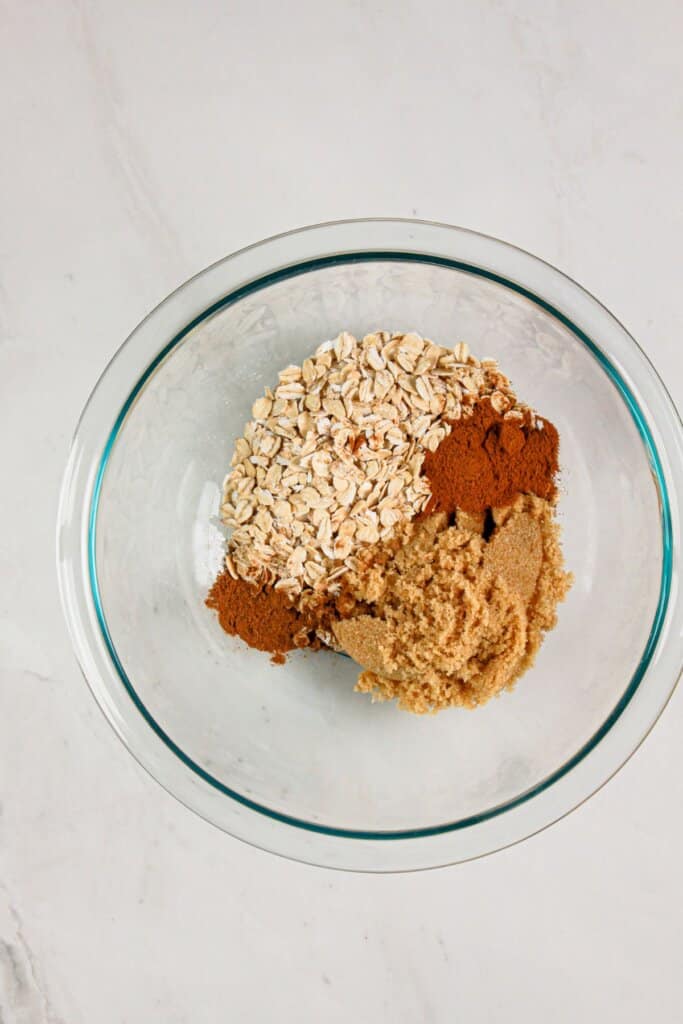 Brown sugar, spices and oats being mixed in a glass bowl.