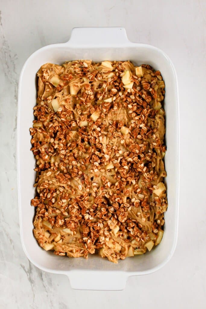 Topping being sprinkled on top of a dessert in a baking dish.