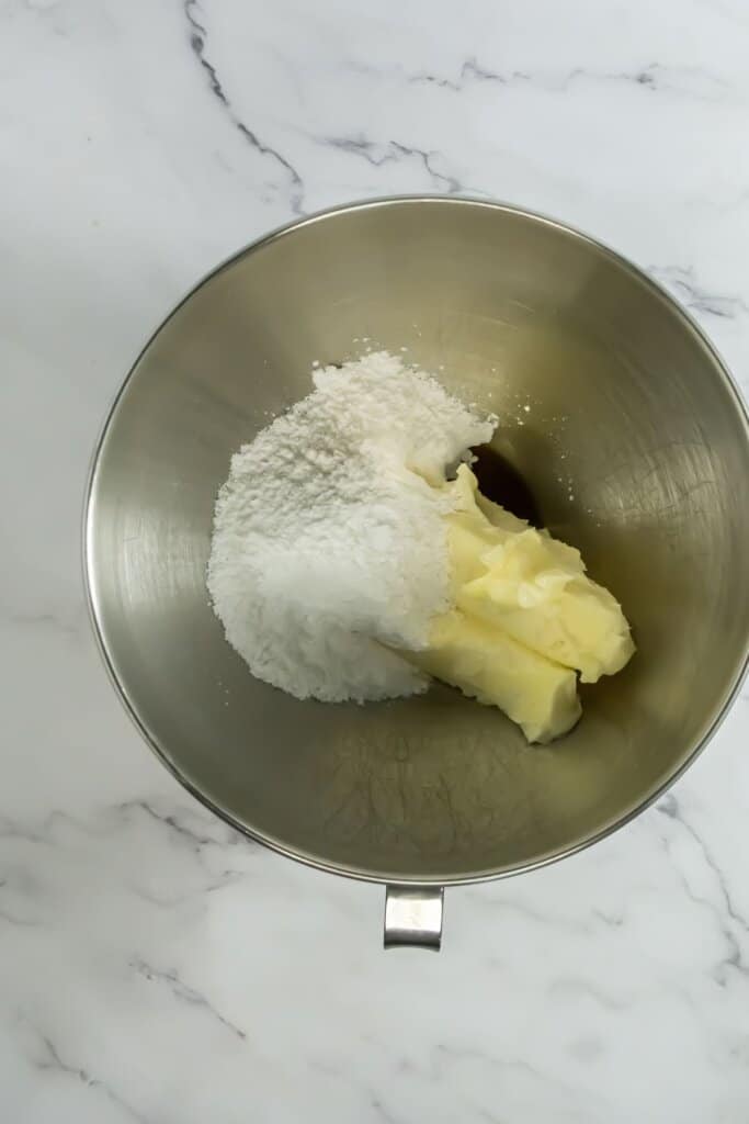 Butter and sugar being mixed together in a stainless steel mixing bowl.