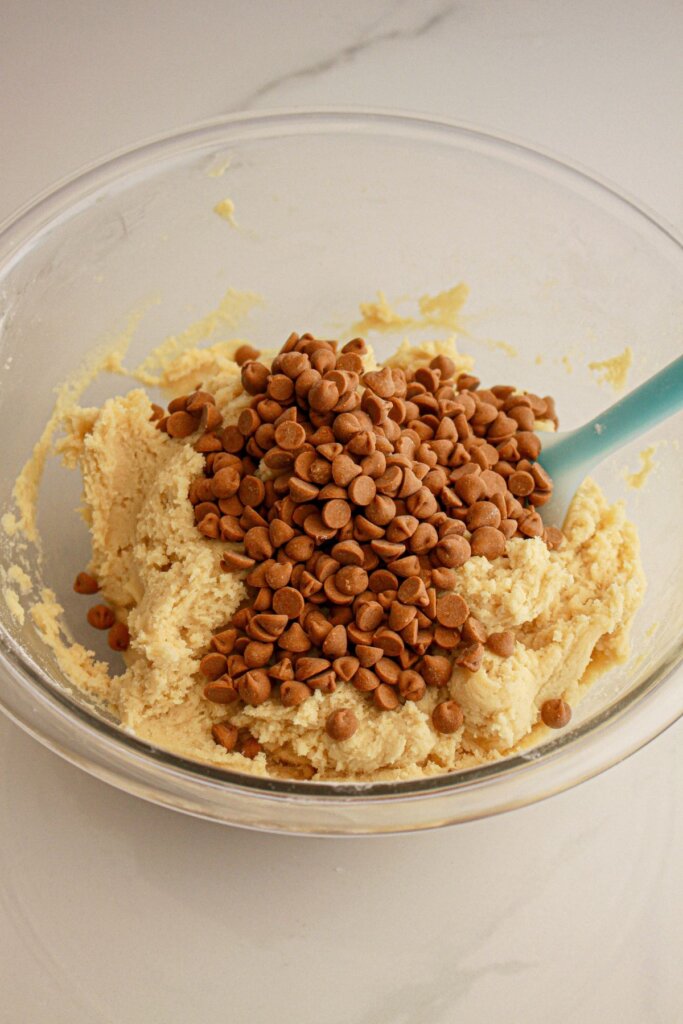 Chips being stirred into dough in a glass mixing bowl.