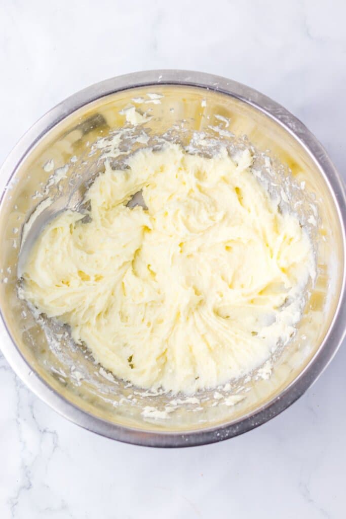 Cream cheese and sugar being mixed in a stainless steel bowl.