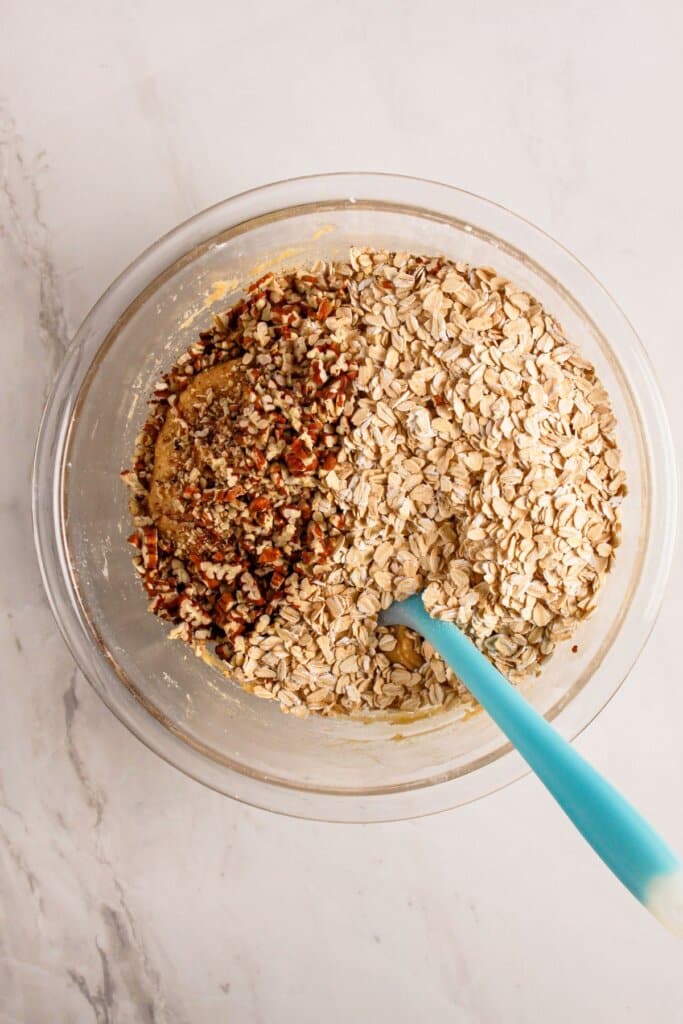 Oats and pecans being stirred into a large bowl.