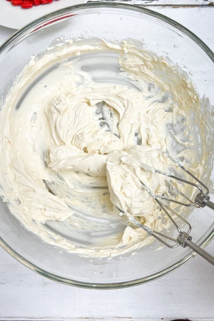 Cream cheese being mixed in a glass bowl.