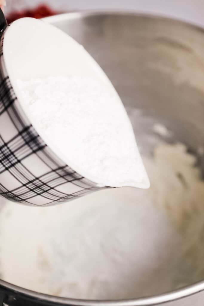 Powdered sugar being added to butter in a bowl.