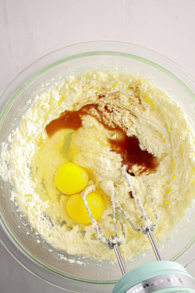 Vanilla and eggs being added to dough in a bowl.