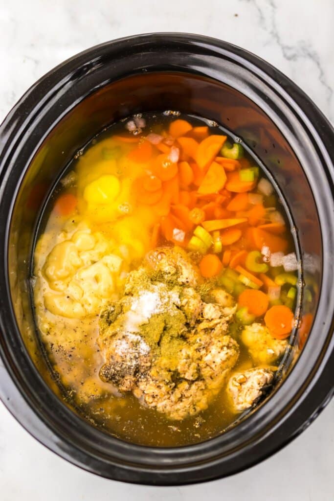 Carrots, seasonings, and soup being added to a crockpot.