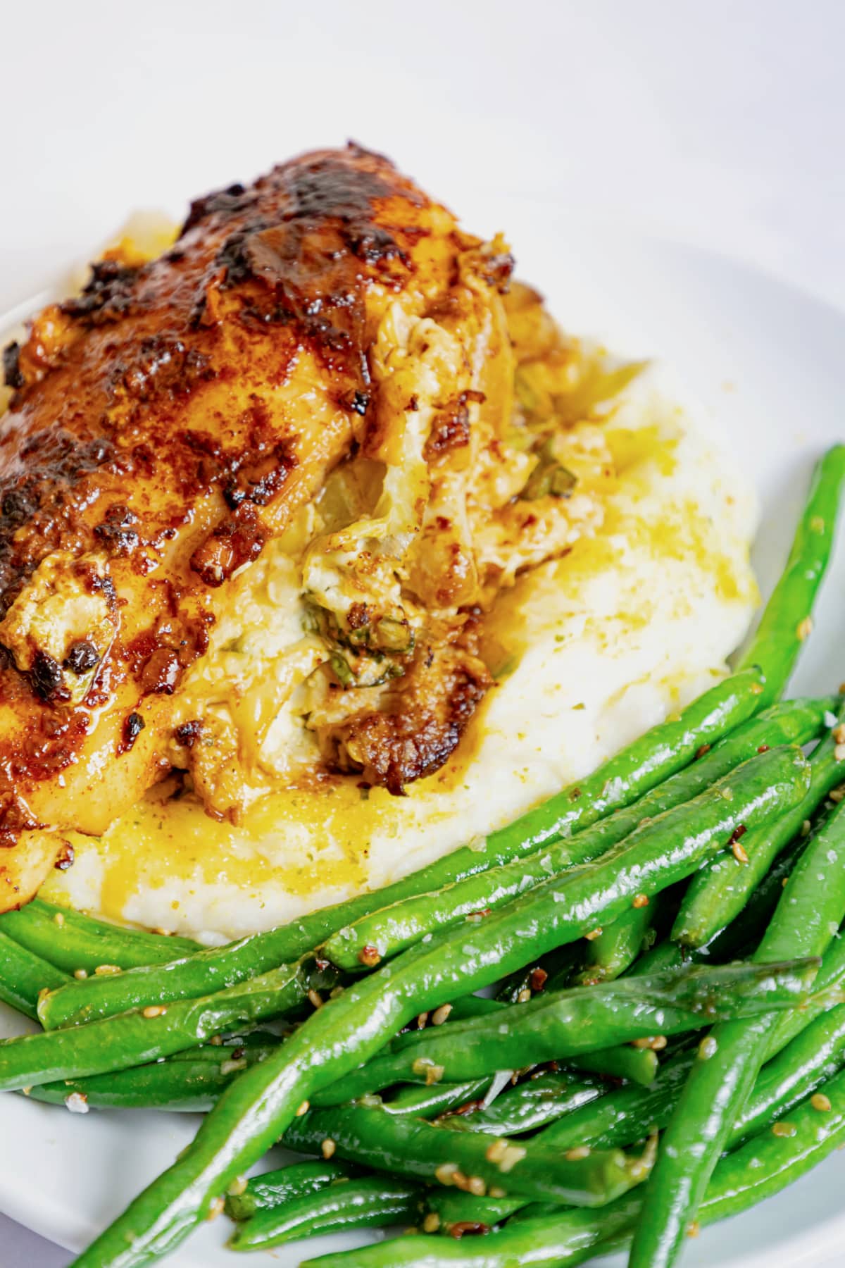 A plate of roasted chicken breast on mashed potatoes with gravy, served with sautéed green beans.