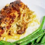 Stuffed chicken breast with herbs and cheese served over mashed potatoes, accompanied by sautéed green beans on a white plate.