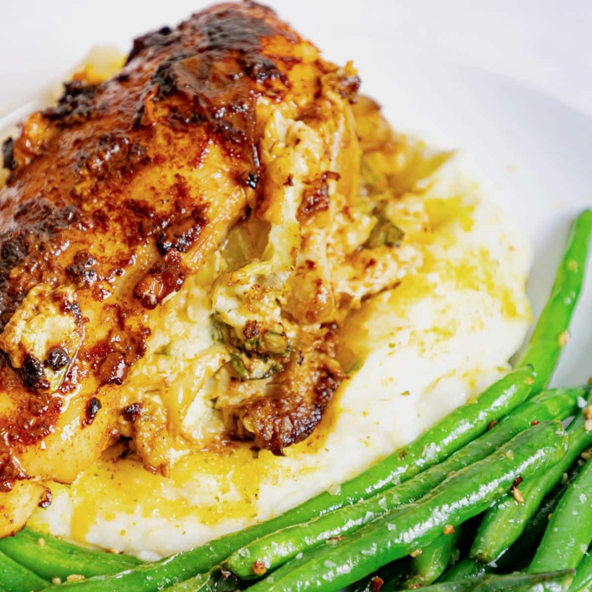 Stuffed chicken breast with herbs and cheese served over mashed potatoes, accompanied by sautéed green beans on a white plate.