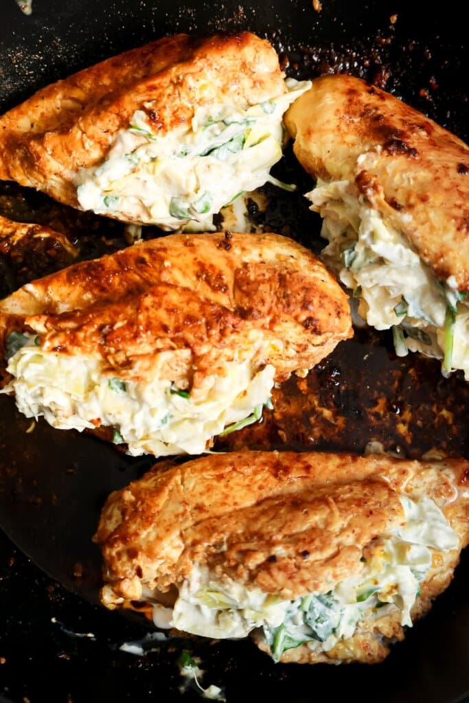 Four seasoned chicken breasts stuffed with a creamy mixture of spinach and cheese are cooking in a skillet.