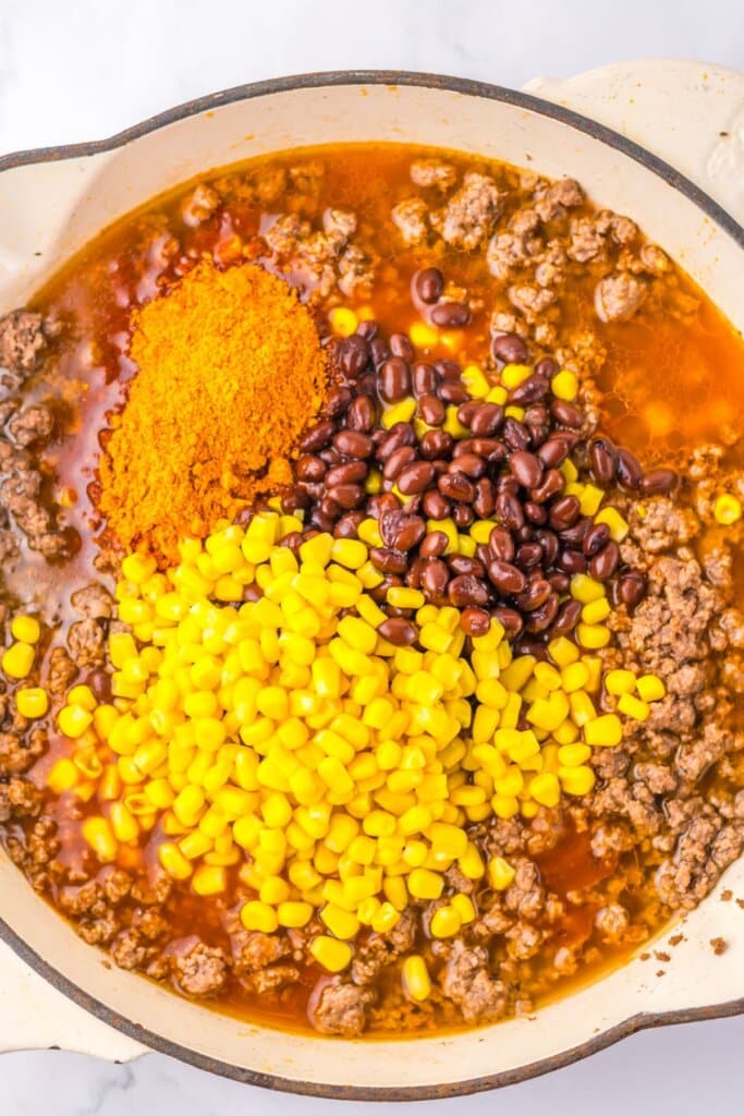 Corn, black beans, and seasoning being added to a pot.
