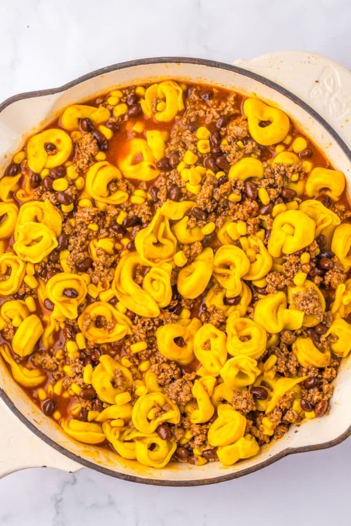 Pasta being added to pot of meat and beans.