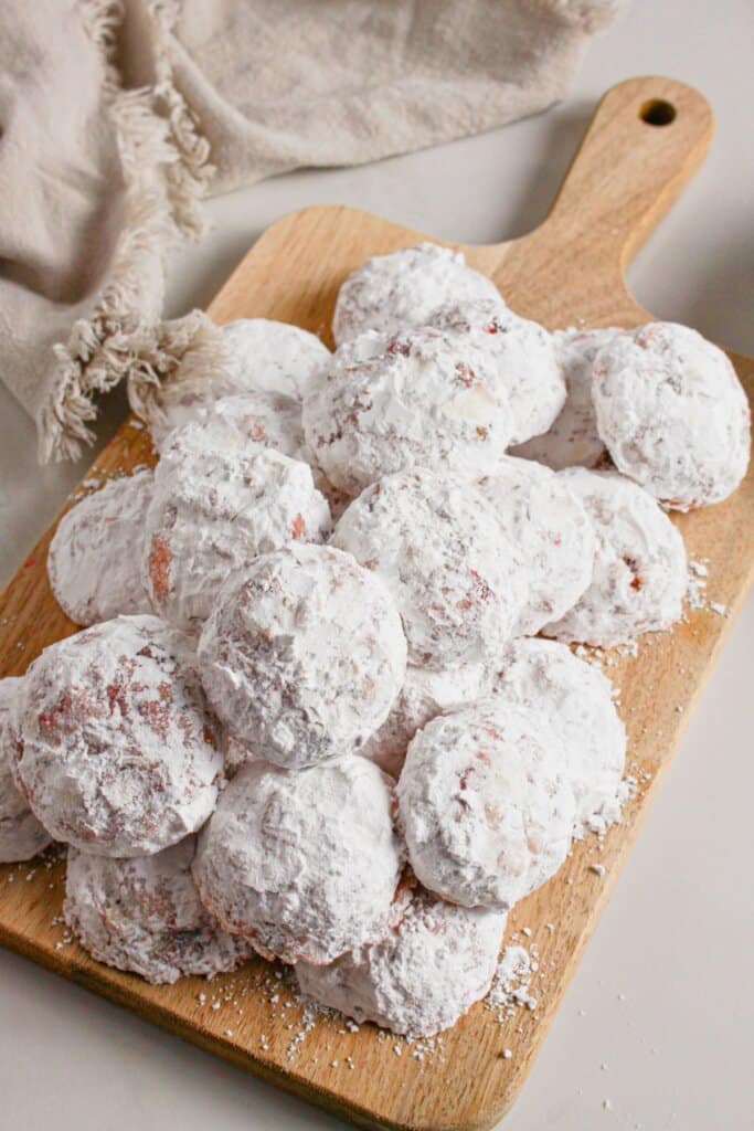 Cherry snowball cookies on a wooden cutting board.