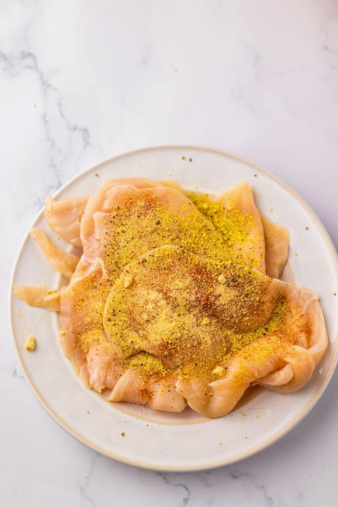 Chicken breasts being seasoned on a plate.