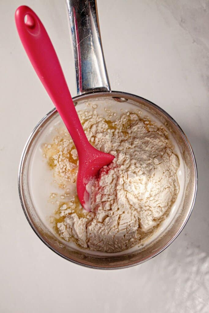 Flour being added to dough in a saucepan.