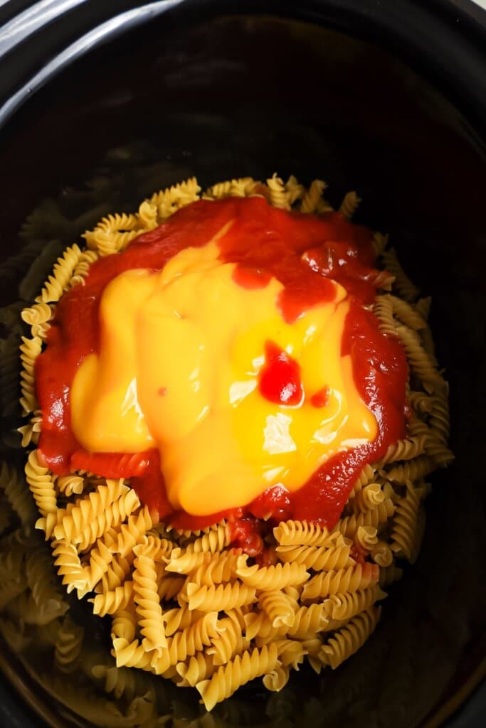 Sauce being added to the top of pasta in a slow cooker.