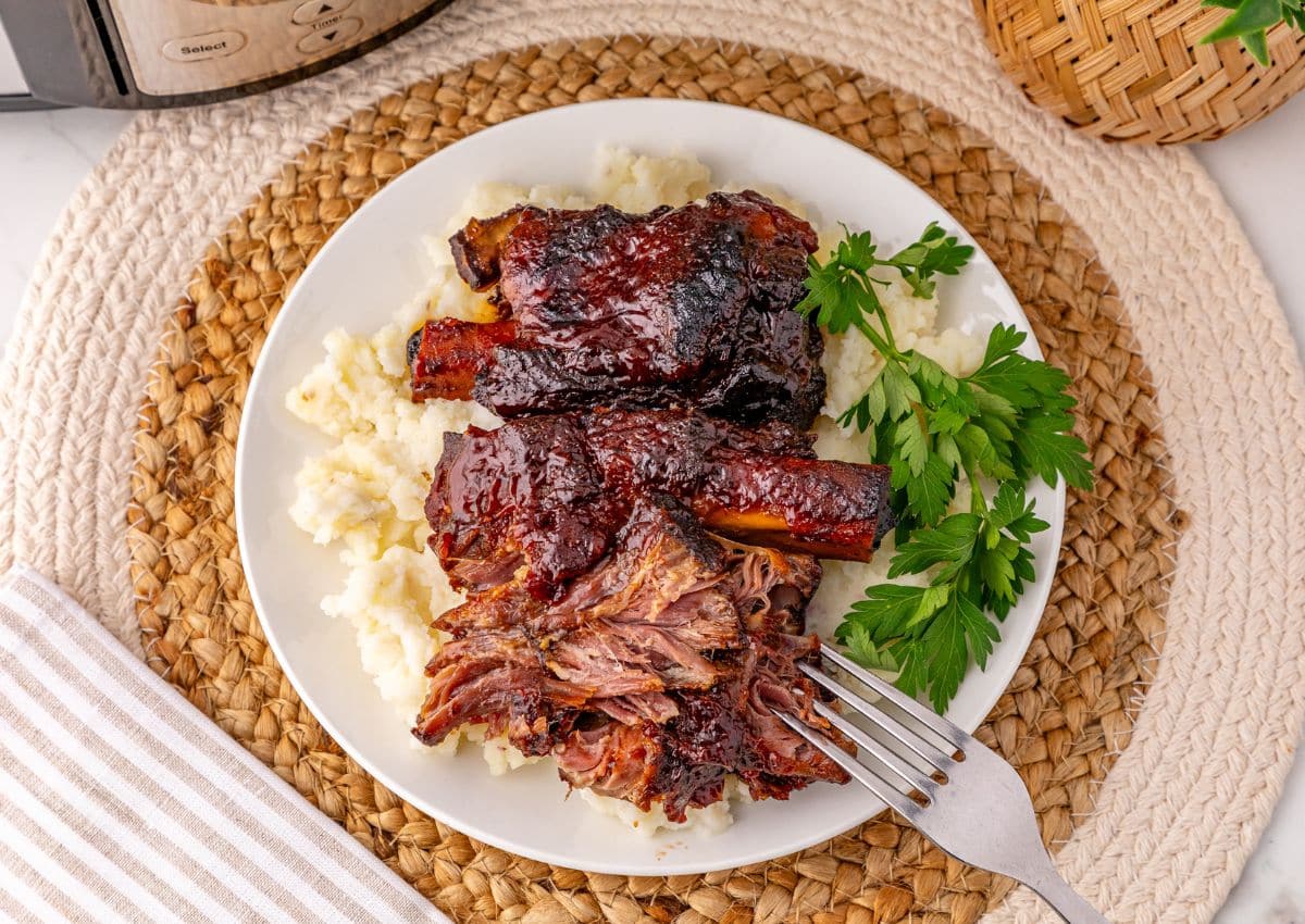 BBQ ribs on top of a bed of mashed potatoes on a plate.
