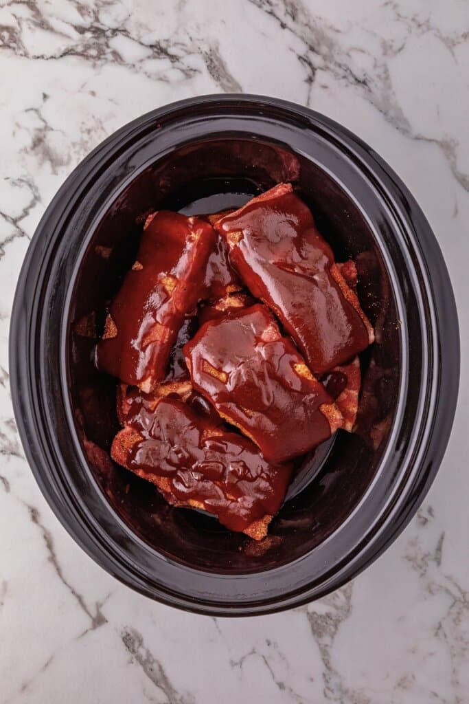 Ribs coated in sauce in a slow cooker.