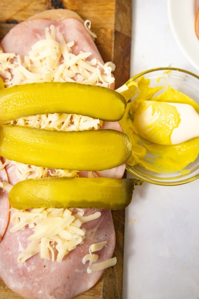 Pickles being added to the top of meat and cheese.