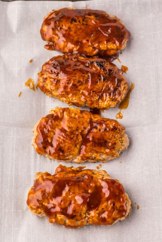 BBQ being spread on pork patties.