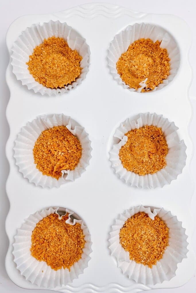Graham cracker crumbs being pressed into a muffin pan.
