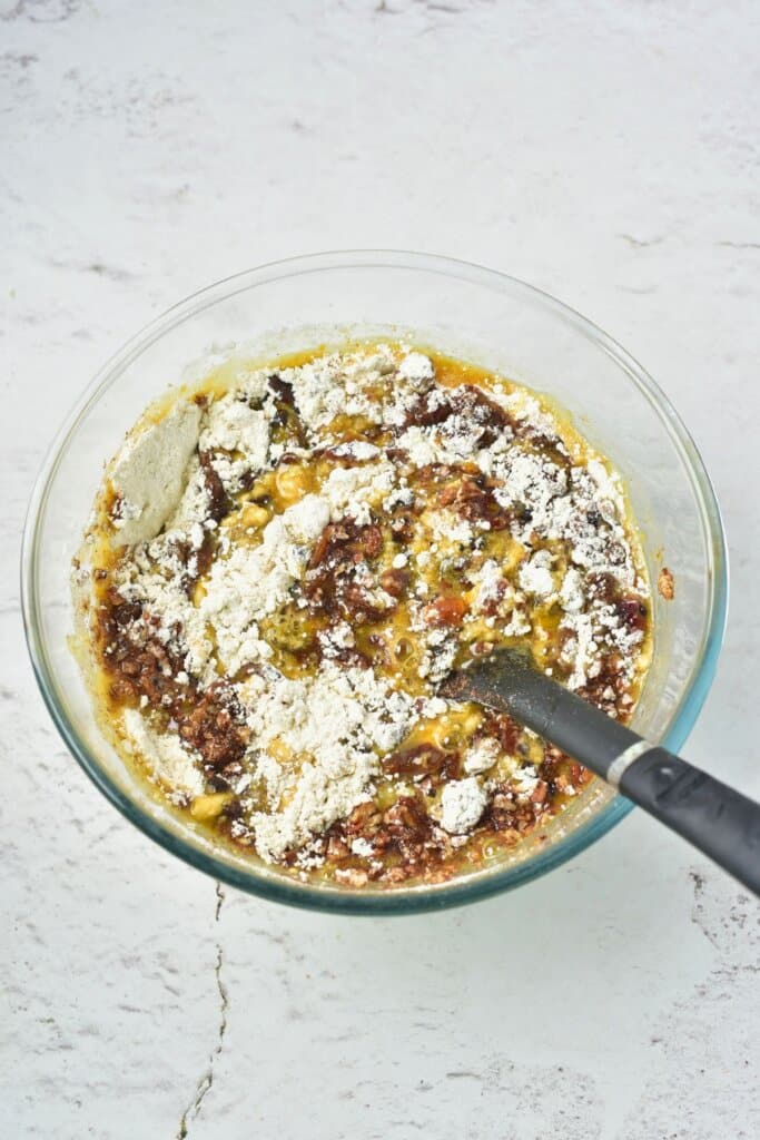 Dry ingredients being added to batter in a glass bowl.