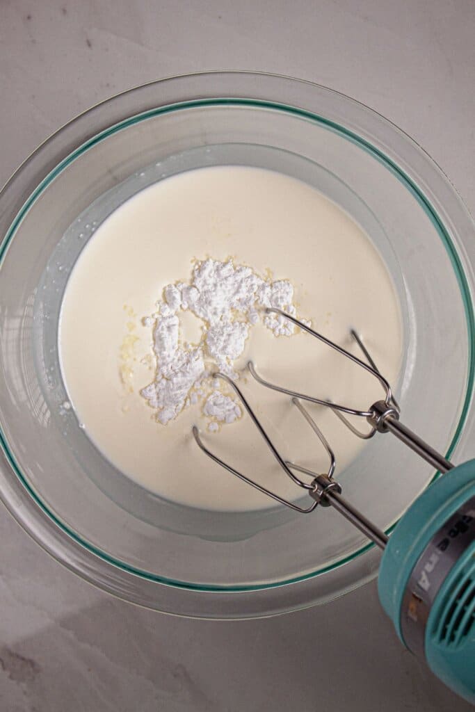 Heavy cream and powdered sugar being whipped in a glass bowl.