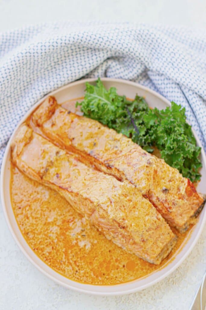 Two salmon filets in cream sauce on a plate.