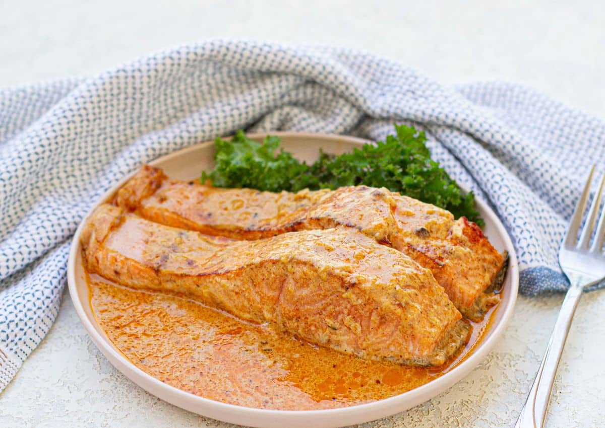 Two salmon filets in cream sauce on a plate.