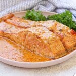 Two salmon filets in cream sauce on a plate.
