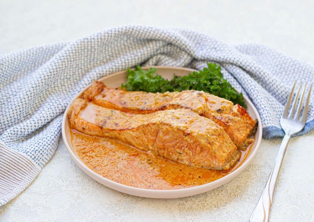 Two salmon filets in cream sauce on a plate.
