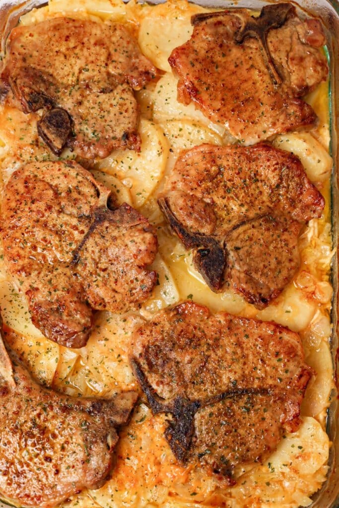 Pork chop on top of a bed of scalloped potatoes.