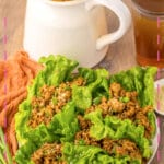 Lettuce cups filled with chicken on a white plate.