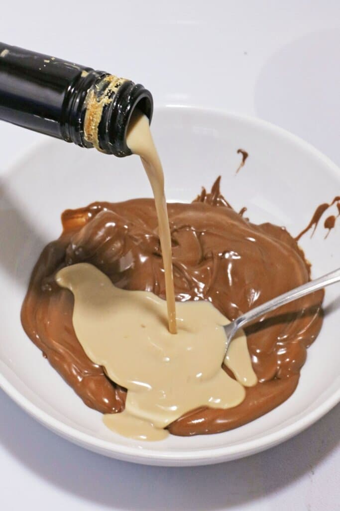 Irish cream being added to melted chocolate in a white bowl.